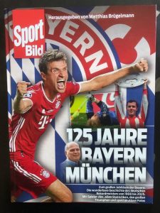 Cover des Buchs "125 Jahre Bayern München", mit dem Bild eines jubelnden Thomas Müller und des Wappens des Vereins im Hintergrund.